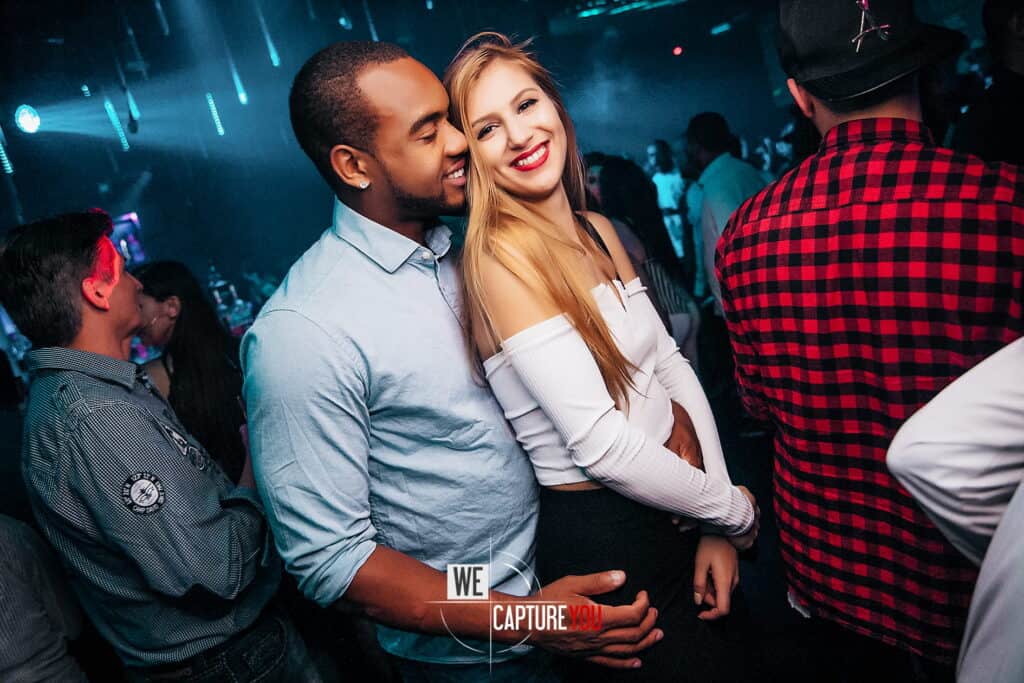 Happy couple enjoying nightlife at a vibrant nightclub with colorful lights.