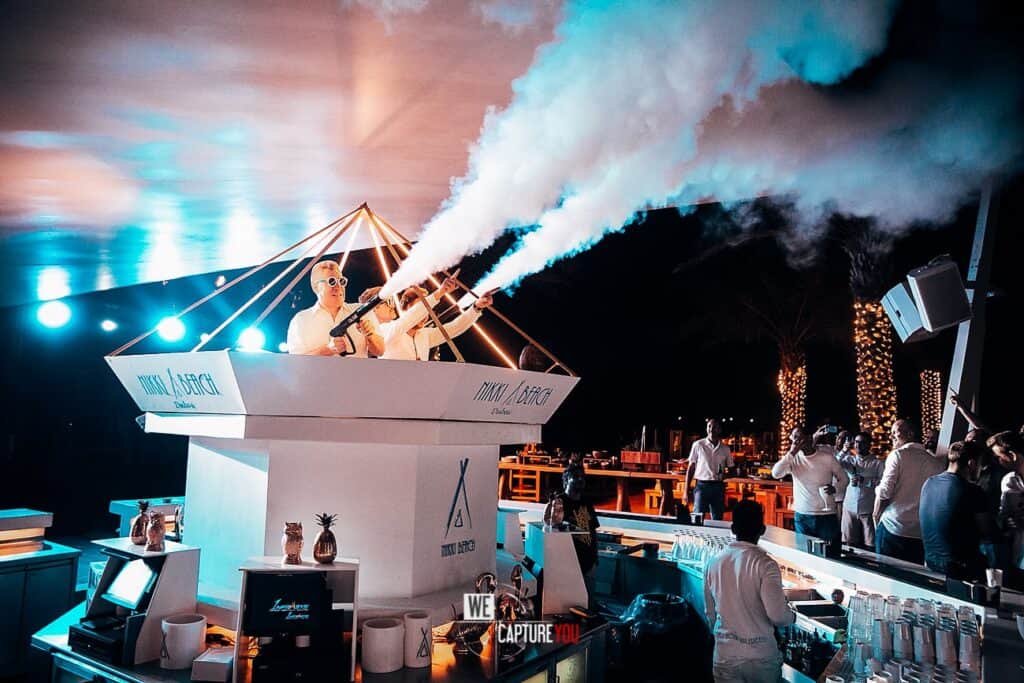 DJ performing at a nightclub with smoke effects and vibrant lighting.