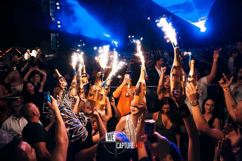 People celebrating with sparklers and champagne bottles at a lively party.