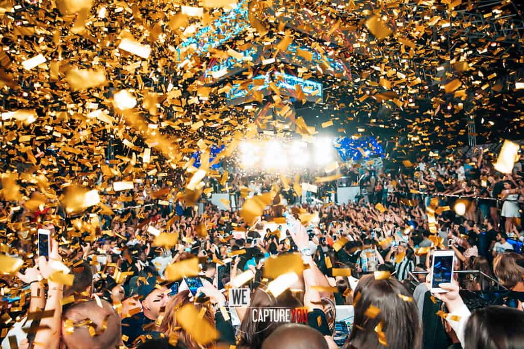 Crowd celebrating at WeCapture event with gold confetti and bright stage lights.