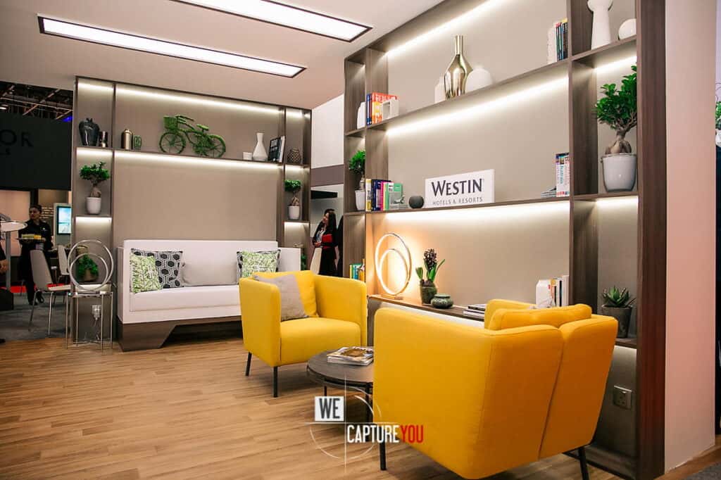 Contemporary hotel lobby with yellow chairs, white sofa, and decorative shelves.