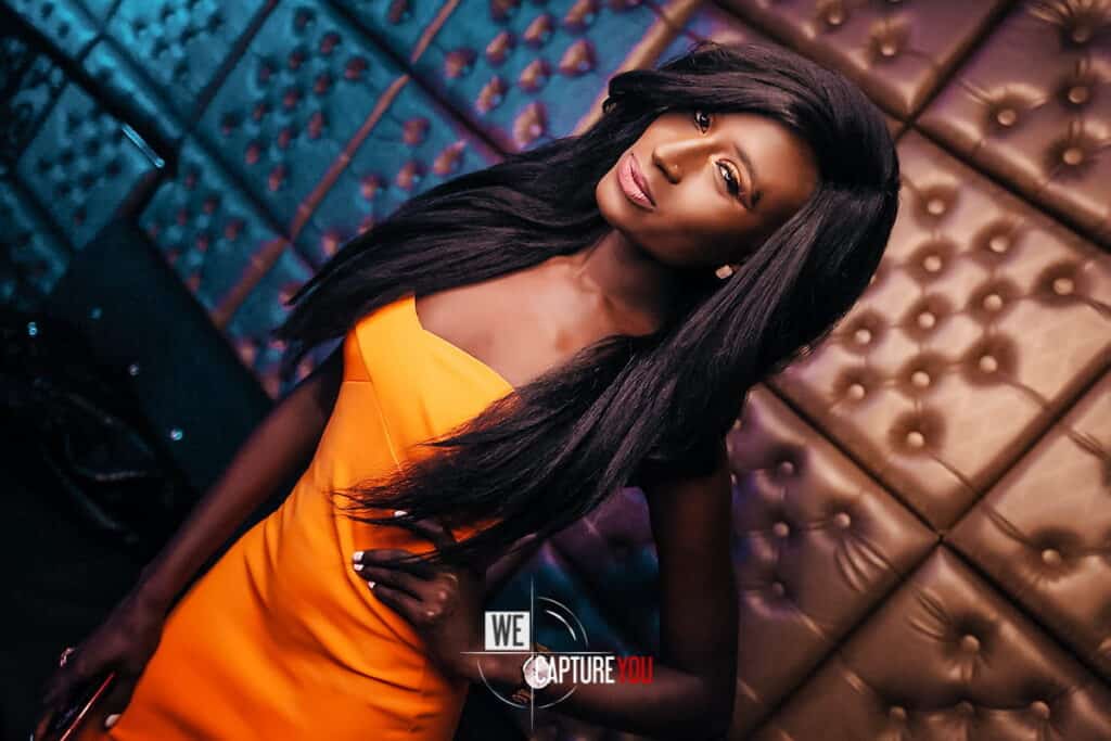 Fashionable woman with long black hair in orange dress at WeCapture event.