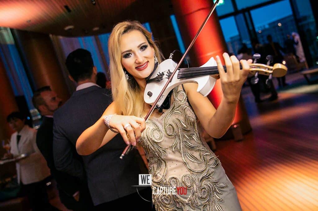 Woman playing violin at a social event with guests in the background.