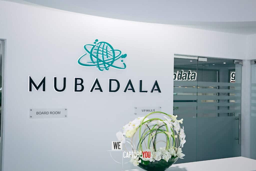 Modern Mubadala office entrance with logo and floral arrangement.