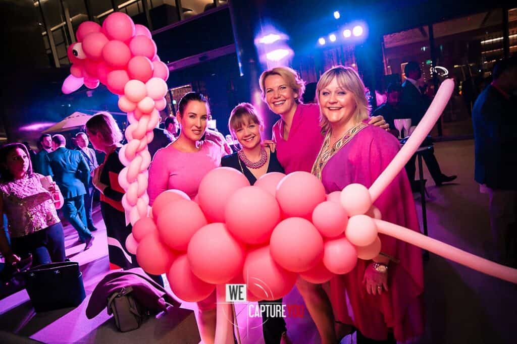 Group of women at a vibrant event with pink balloon decorations and colorful lighting.