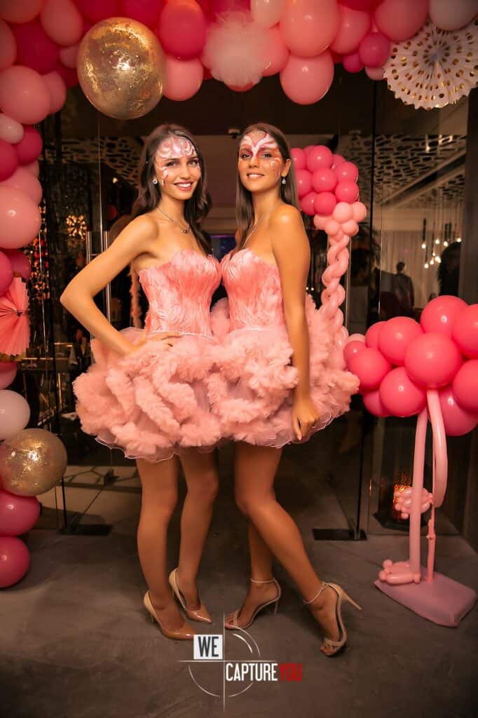 Two women in pink dresses at a festive event with balloons and decorations.