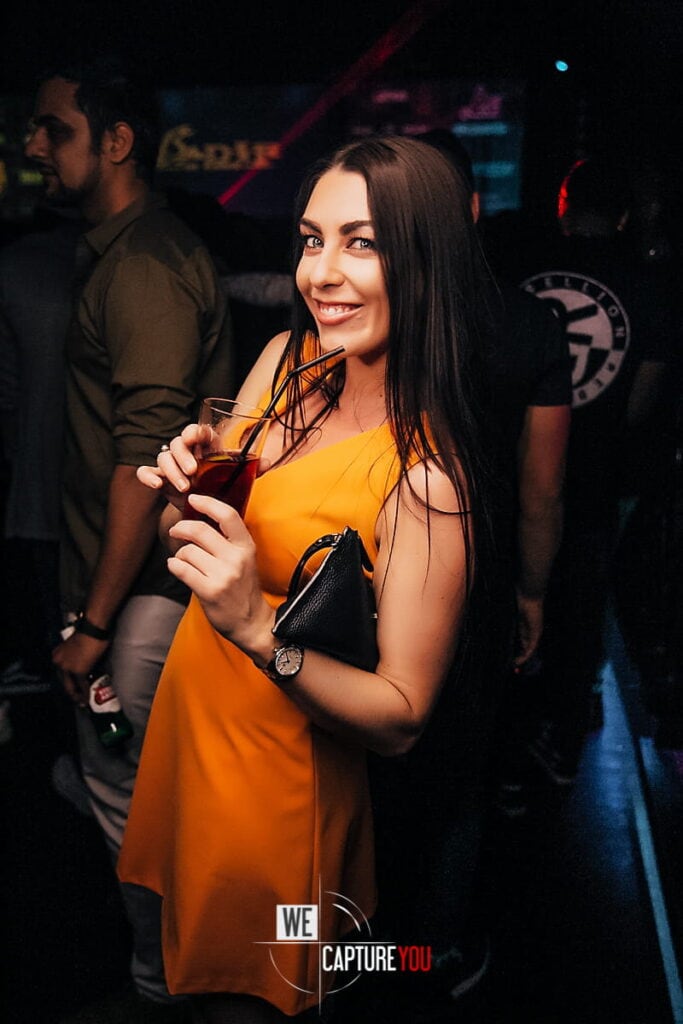 Young woman in yellow dress enjoying drinks at a nightclub.