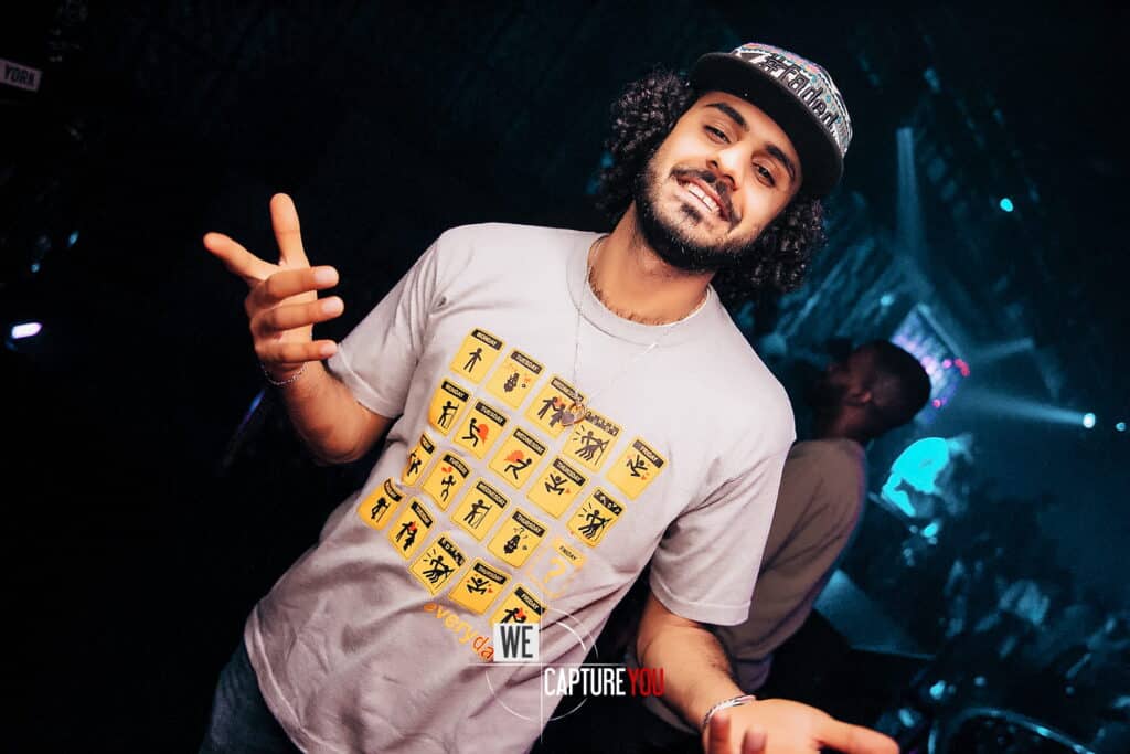 Happy man with curly hair and a cap dancing at a nightclub.