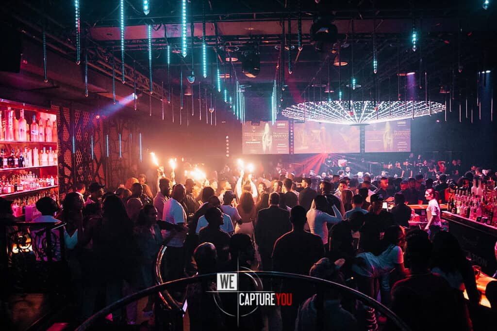 Crowd dancing at a lively nightclub with colorful lights and stage effects.