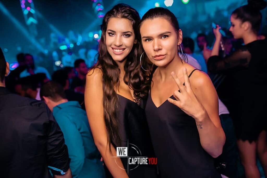Two women enjoying a night out at a lively nightclub with colorful lights.