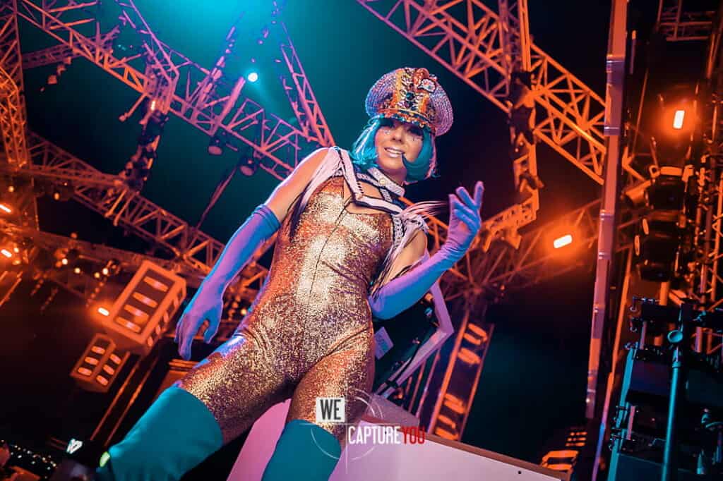 Performer in colorful costume on stage with dynamic lighting at WeCapture event.