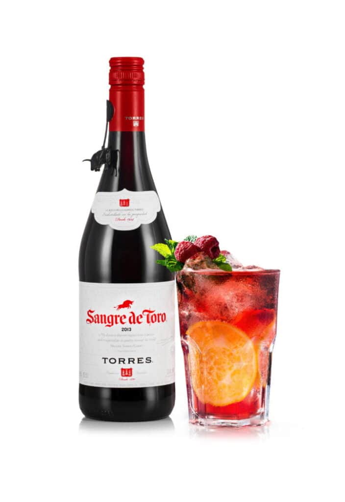 Bottle of Sangre de Toro red wine next to a berry cocktail with fruit garnish.