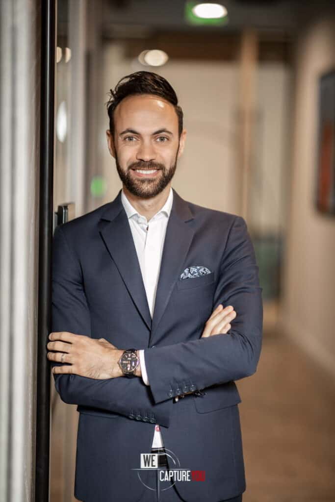 Confident businessman in a suit smiling in an office corridor.