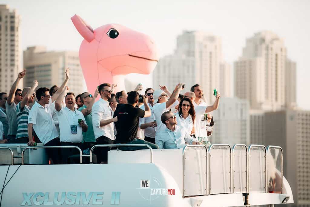 Group of people celebrating on a boat with a pink inflatable horse head in the background.