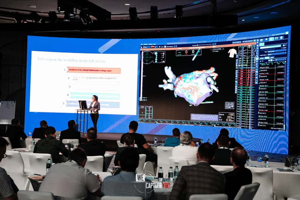 Conference presentation with digital screens showing data and 3D models.