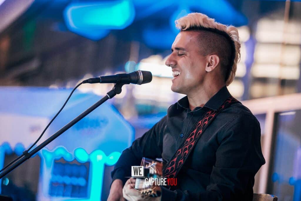 Male singer with a guitar singing into a microphone at night.