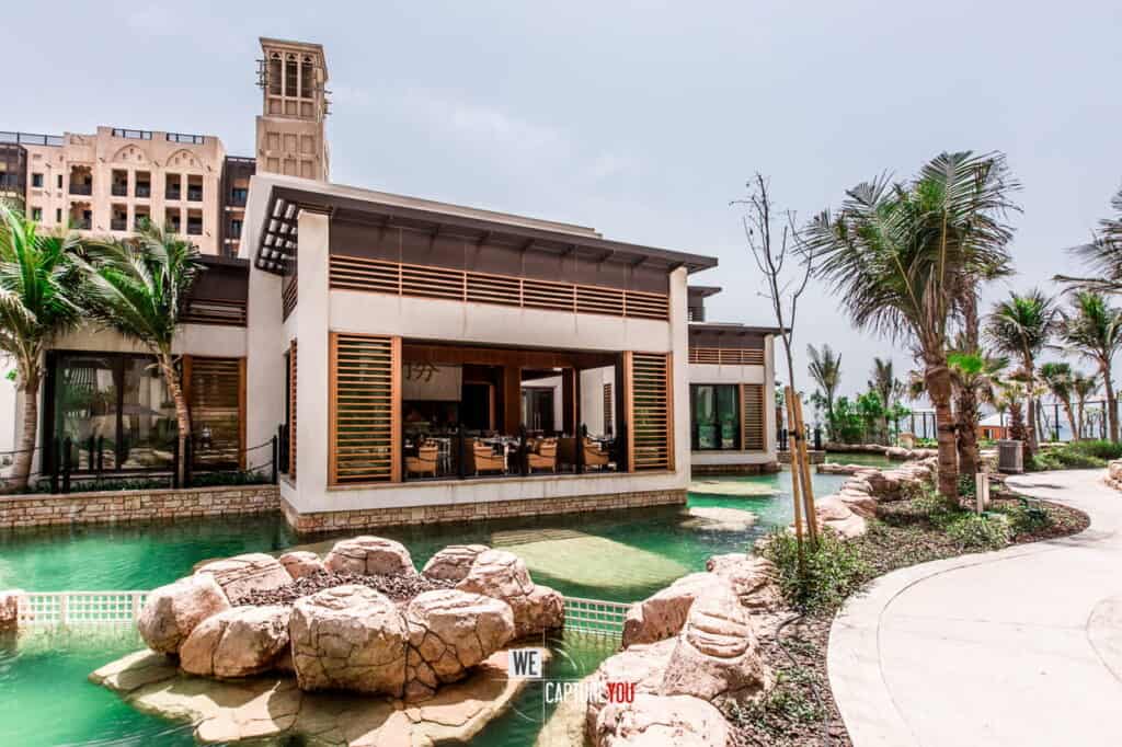 Modern luxury resort with pool, palm trees, and tropical landscaping.