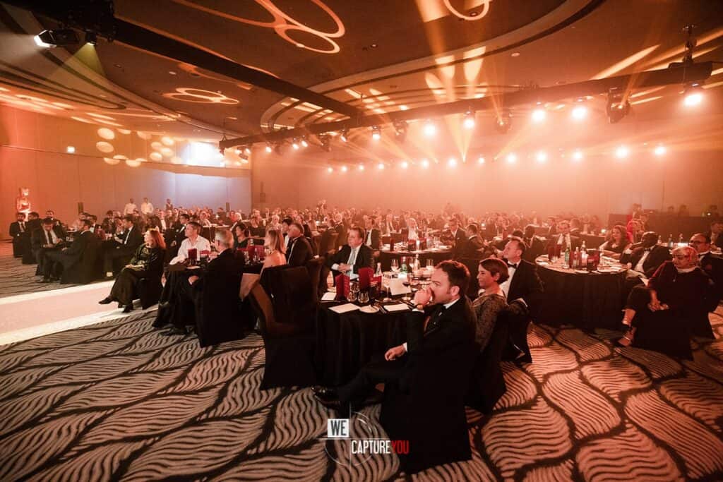 Large conference hall with attendees seated at tables during a formal event.