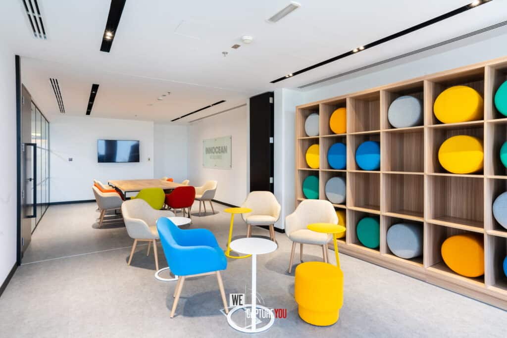 Contemporary office lounge with vibrant chairs and a wooden storage unit.