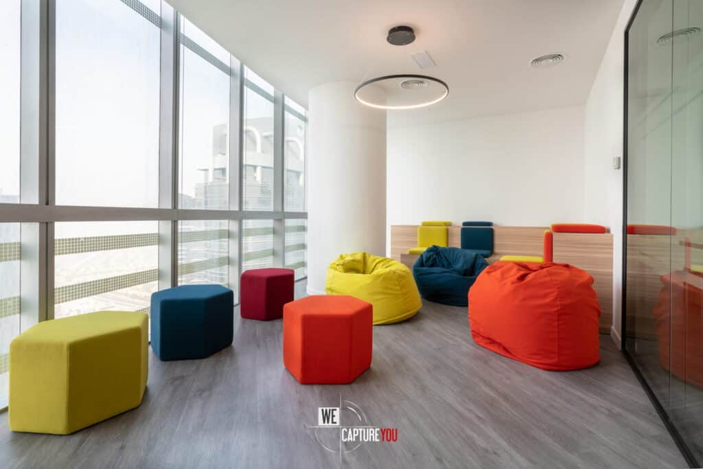 Bright office lounge with colorful bean bags and stools near large windows.