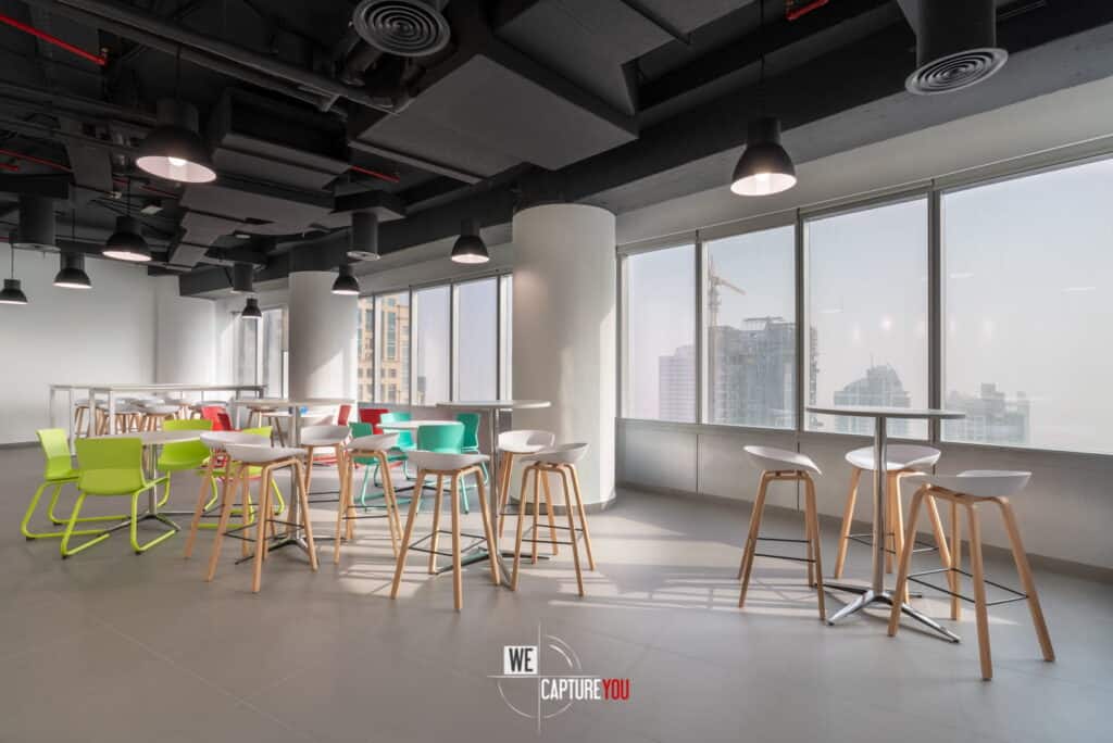 Bright modern office lounge with colorful chairs and large windows overlooking cityscape.