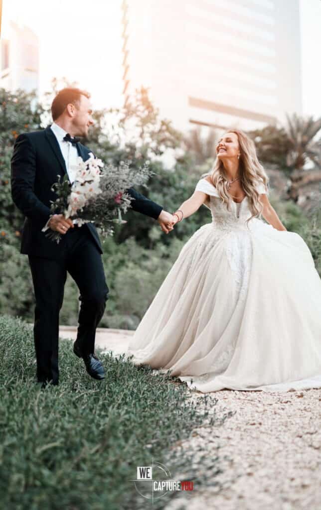 Bride and groom holding hands in a city park with skyscrapers in the background.