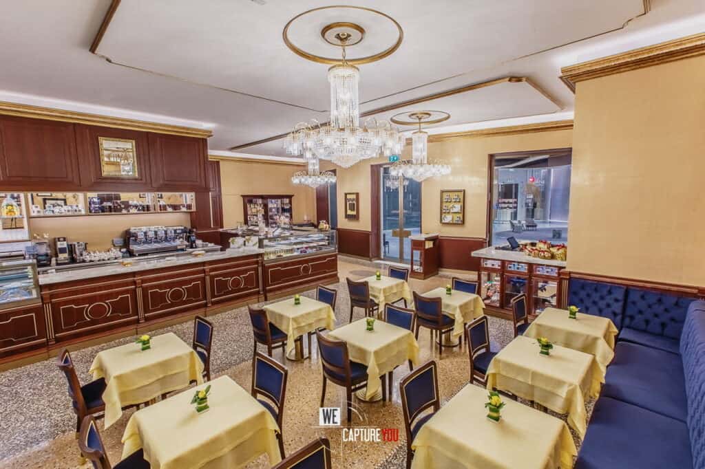 Upscale hotel restaurant with yellow walls, chandeliers, and neatly arranged tables.