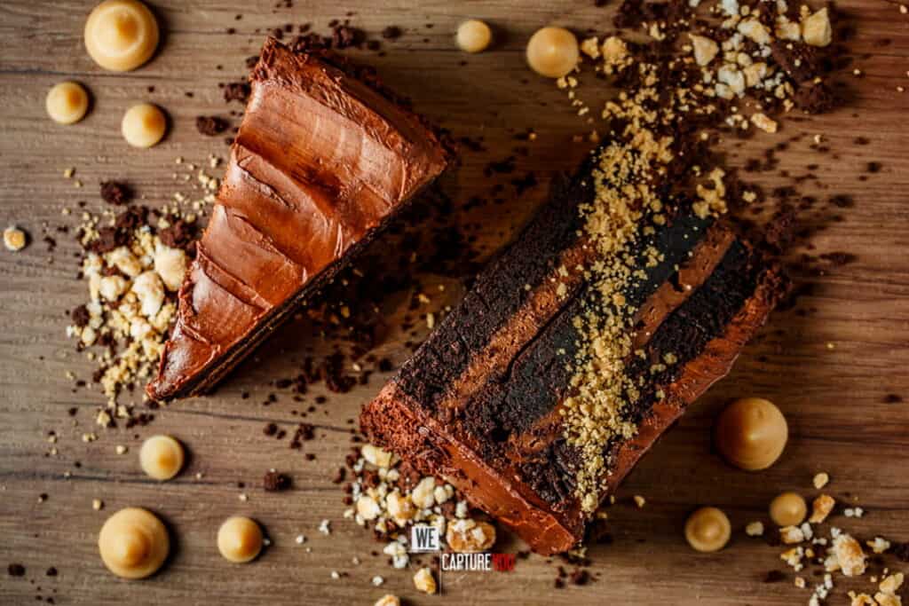 Rich chocolate cake with hazelnuts and chocolate shavings on wooden surface.