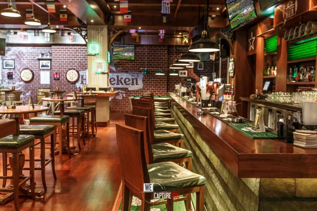 Interior of a sports bar with wooden furniture, bar counter, and multiple TV screens.