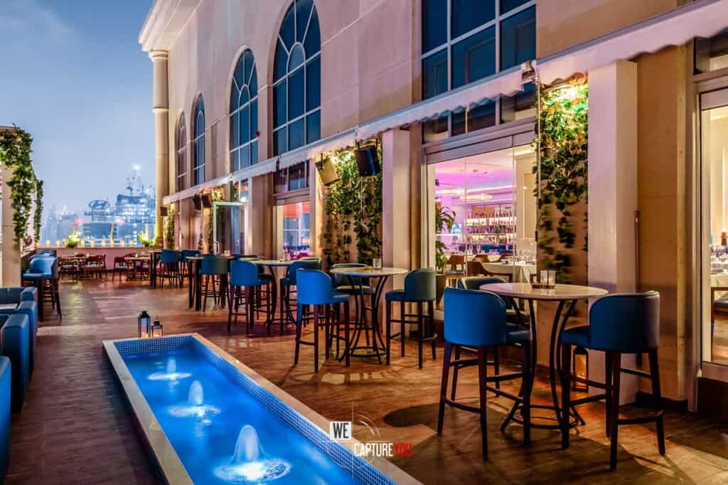 Modern outdoor lounge with bar tables, chairs, and water feature at WeCapture.