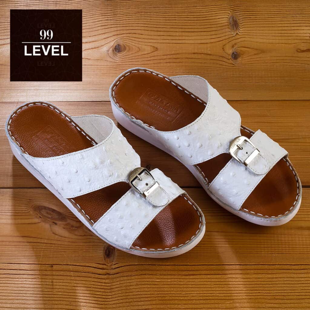 Stylish white leather sandals with buckle on wooden surface.