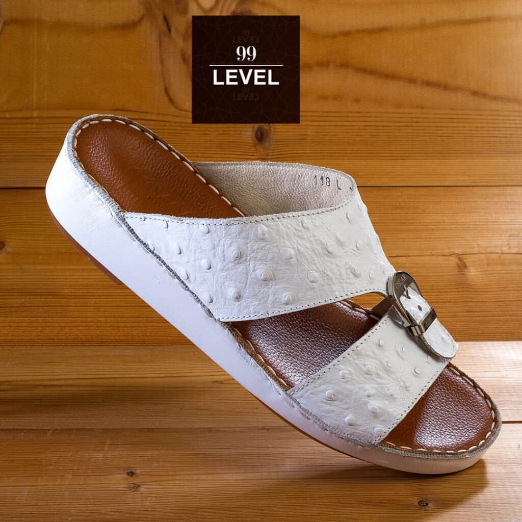 White and brown men's sandal with buckle on wooden surface.