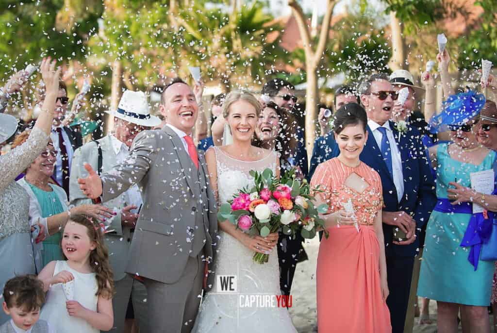 Joyful wedding scene with guests celebrating and throwing confetti.
