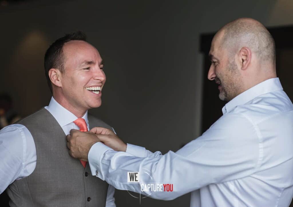Groom and best man adjusting tie before wedding ceremony.