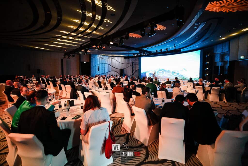 Large conference room with attendees and a big screen presentation.