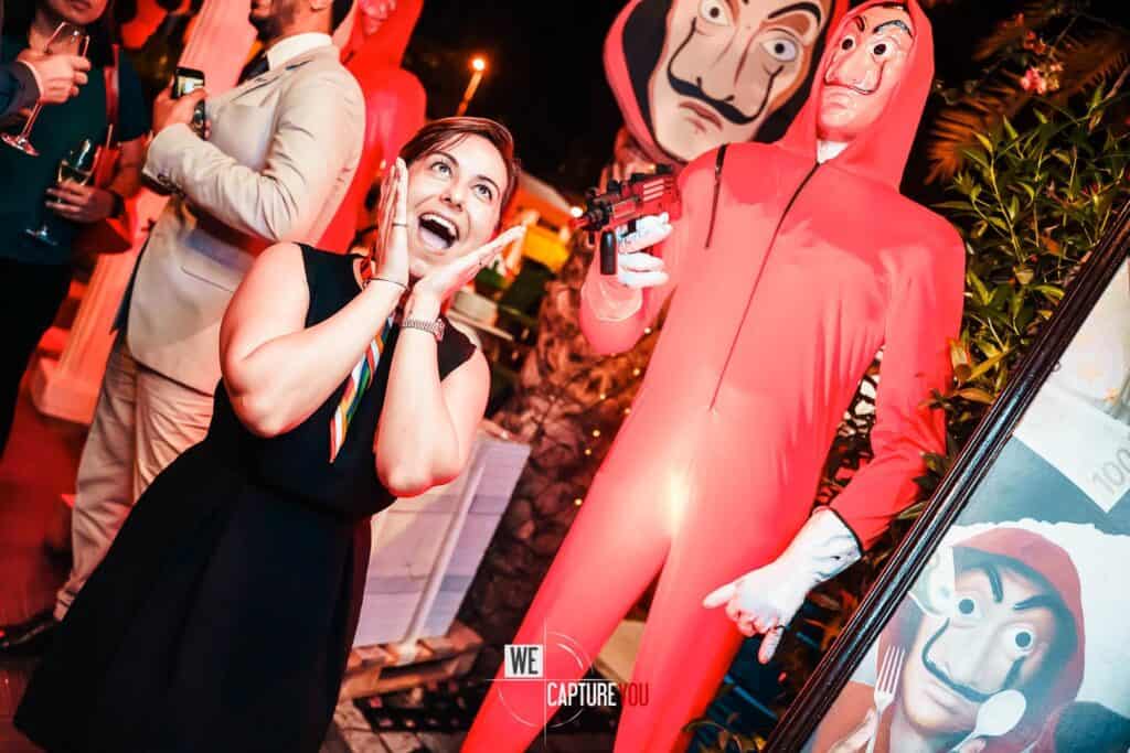 Woman in black dress at Halloween party with creepy characters and decorations.