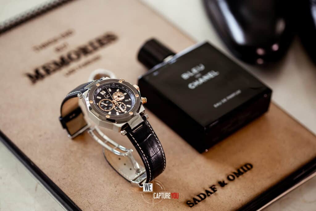 Luxury wristwatch with black leather strap and perfume bottle on memo pad.