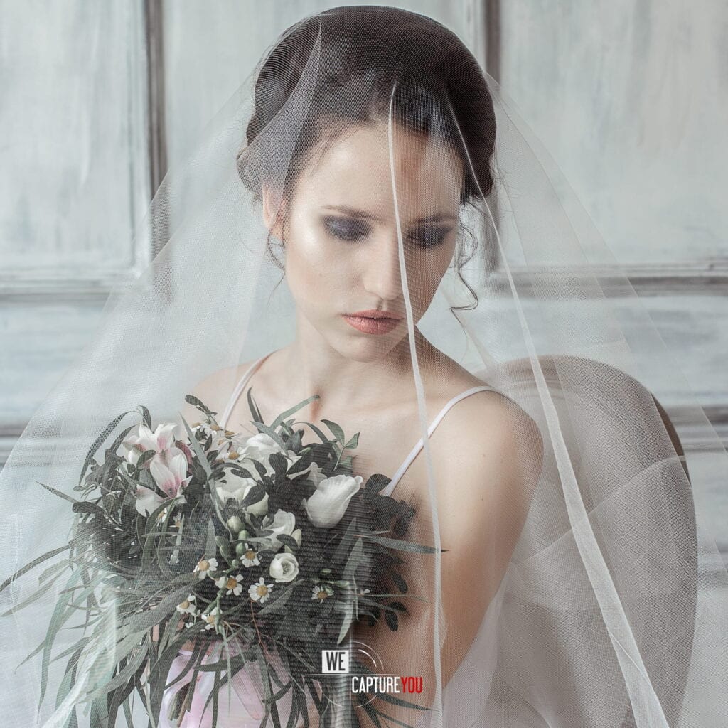 Bride holding a bouquet of flowers with a veil and elegant makeup.