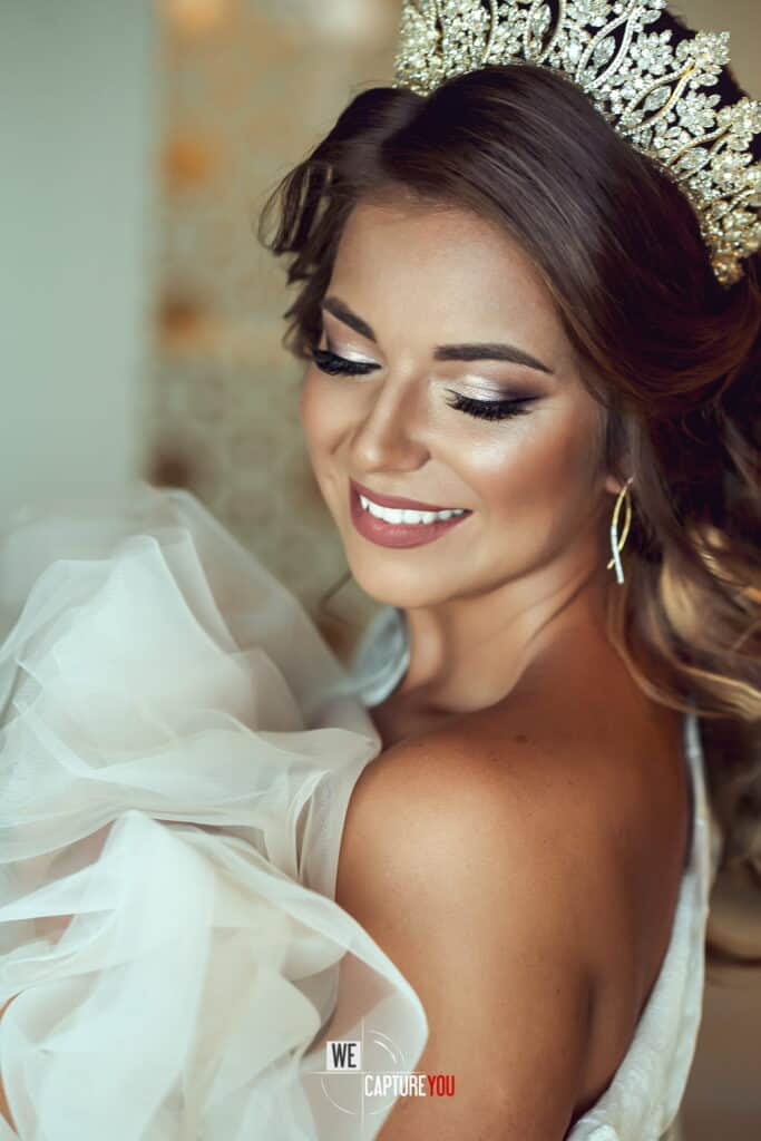Beautiful bride with crown, makeup, and wedding dress, smiling gracefully.