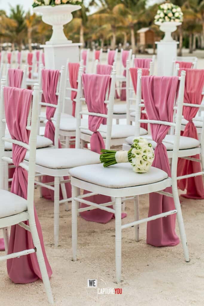 Beach wedding chairs decorated with pink fabric and white flowers.