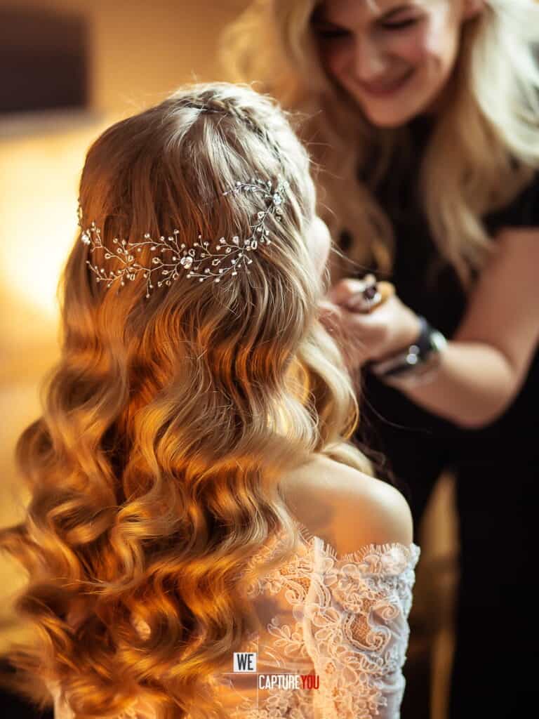 Bride with long, wavy hair and a delicate tiara, smiling with a woman in the background.