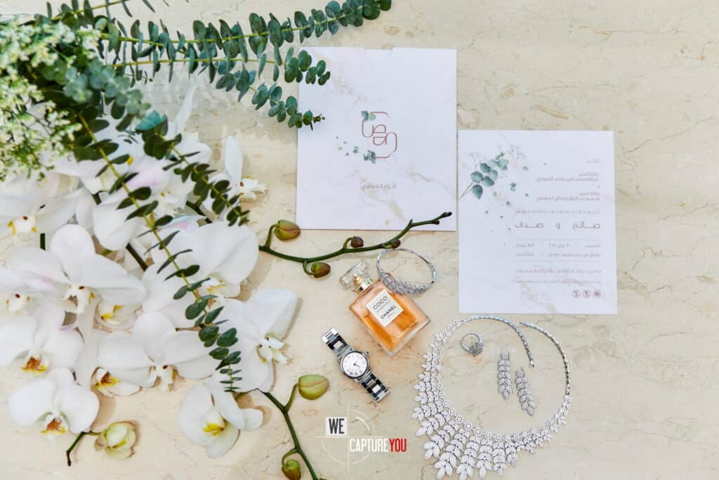 Wedding jewelry, perfume, and invitations arranged on a marble surface.
