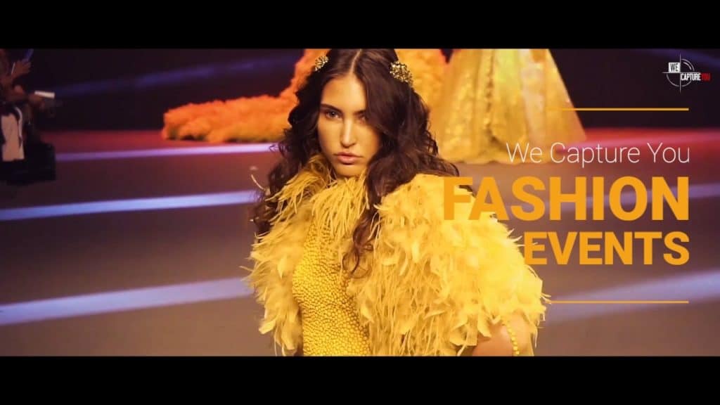 Fashion model walking runway at Dubai fashion event with yellow outfit and feathered accessories.