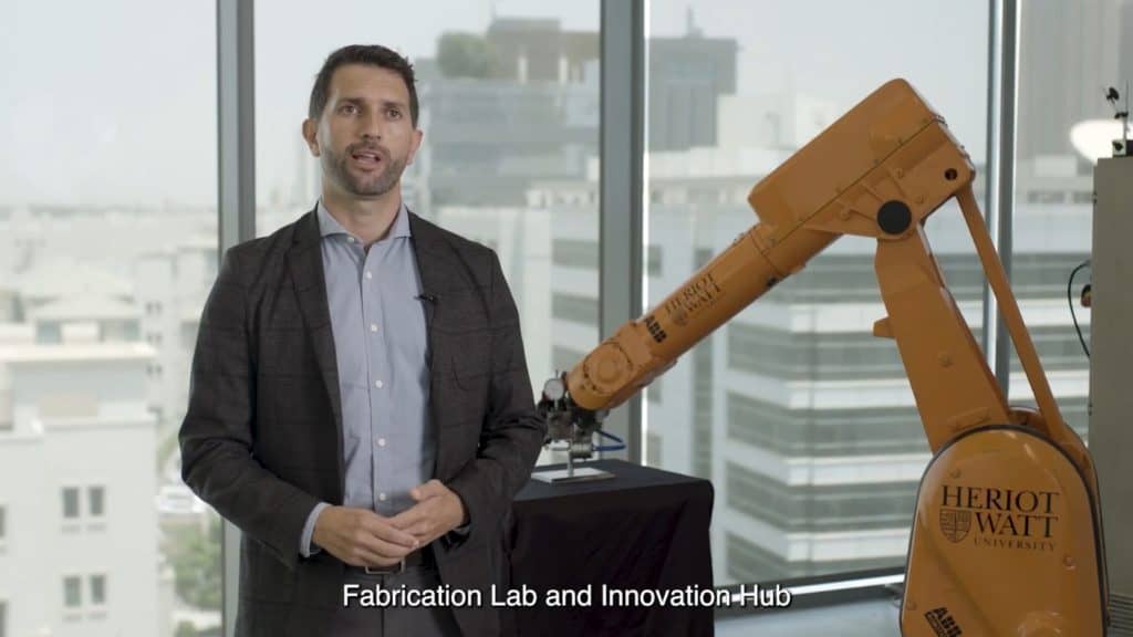 Man presenting in fabrication lab with robotic arm at Heriot Watt University.