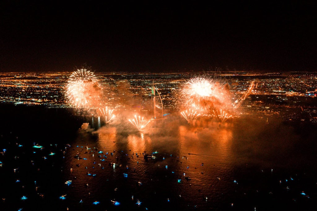 Nighttime Dubai skyline with fireworks over the water during a celebration.