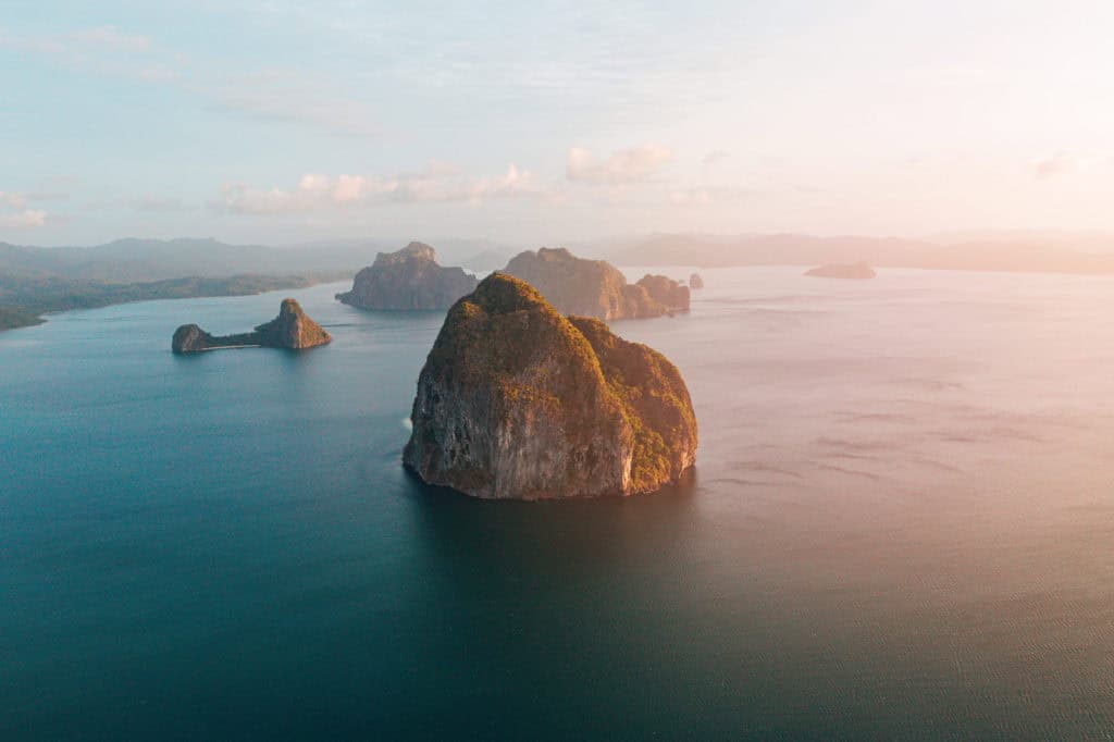 Aerial drone photo of rocky islands in calm ocean at sunset.