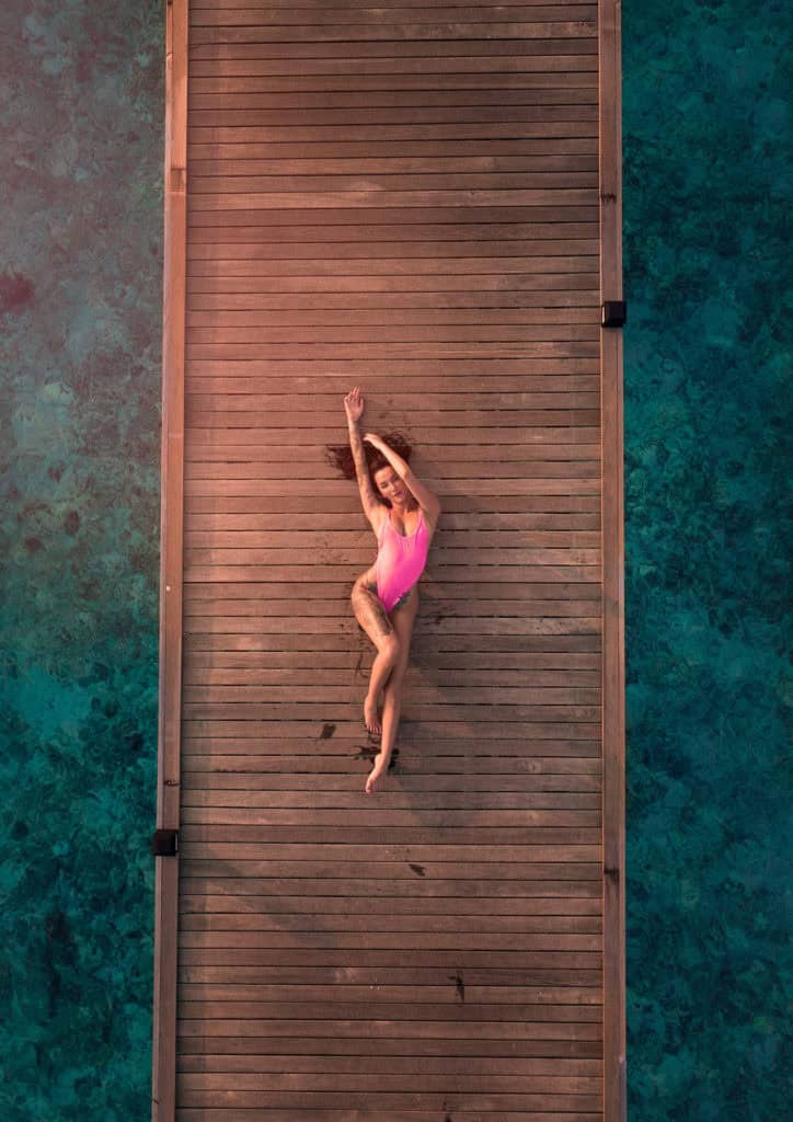 A woman in a pink swimsuit lying on a wooden dock over water.