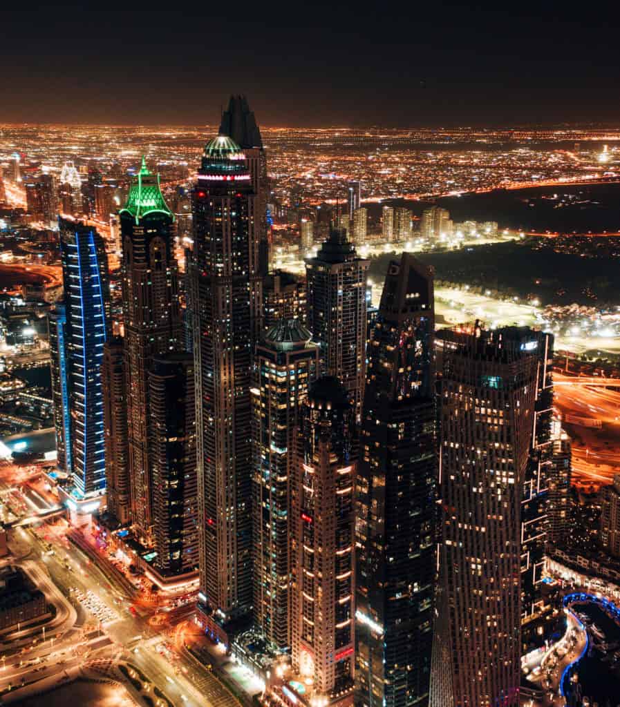 Aerial drone shot of Dubai's illuminated skyscrapers at night.