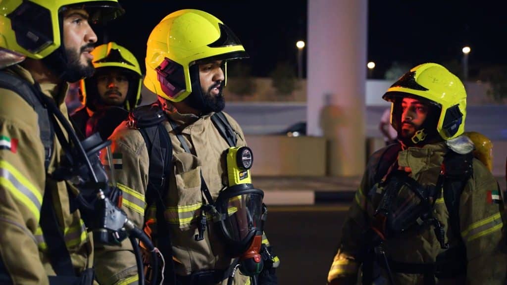 Firefighters in yellow helmets preparing for operation at night in Dubai.