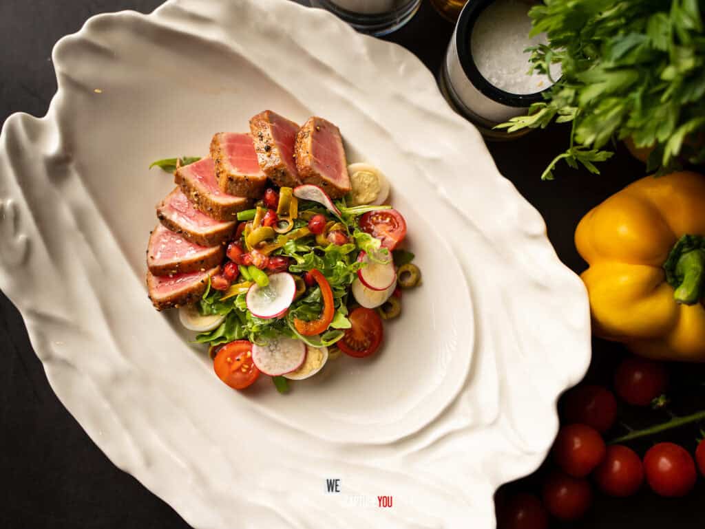 Seared tuna salad with cherry tomatoes, radishes, and mixed greens on a white plate.